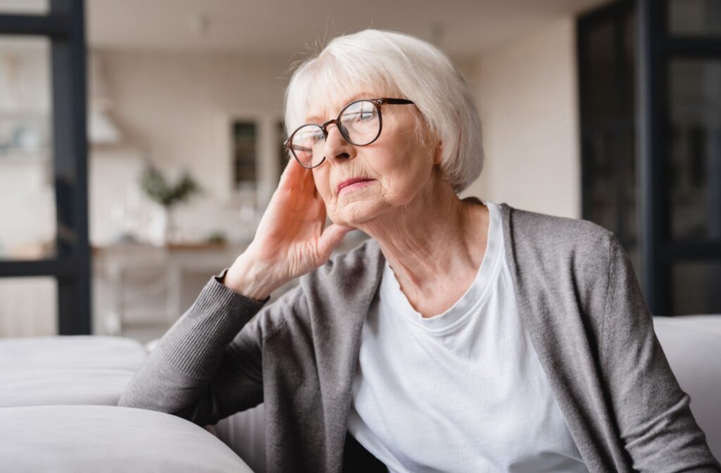 An older adult sits on a couch while thinking about senior living.